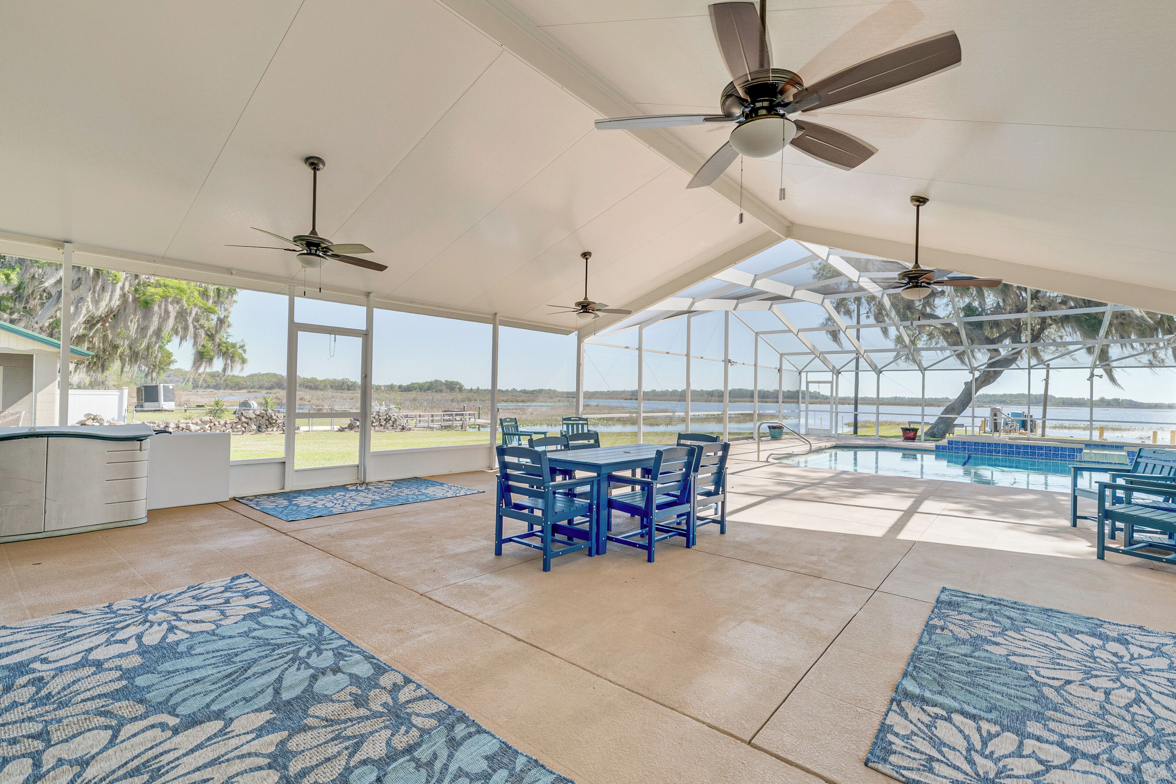 Un espacio al aire libre techado con piscina, mobiliario azul, ventiladores de techo y amplias ventanas.