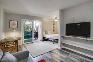 A modern living room with a sofa, a dining table, a TV mounted on the wall, and a sliding glass door leading to an outdoor area. - San Diego Studio w/ Pool Access, 2 Mi to Old Town! (San Diego)