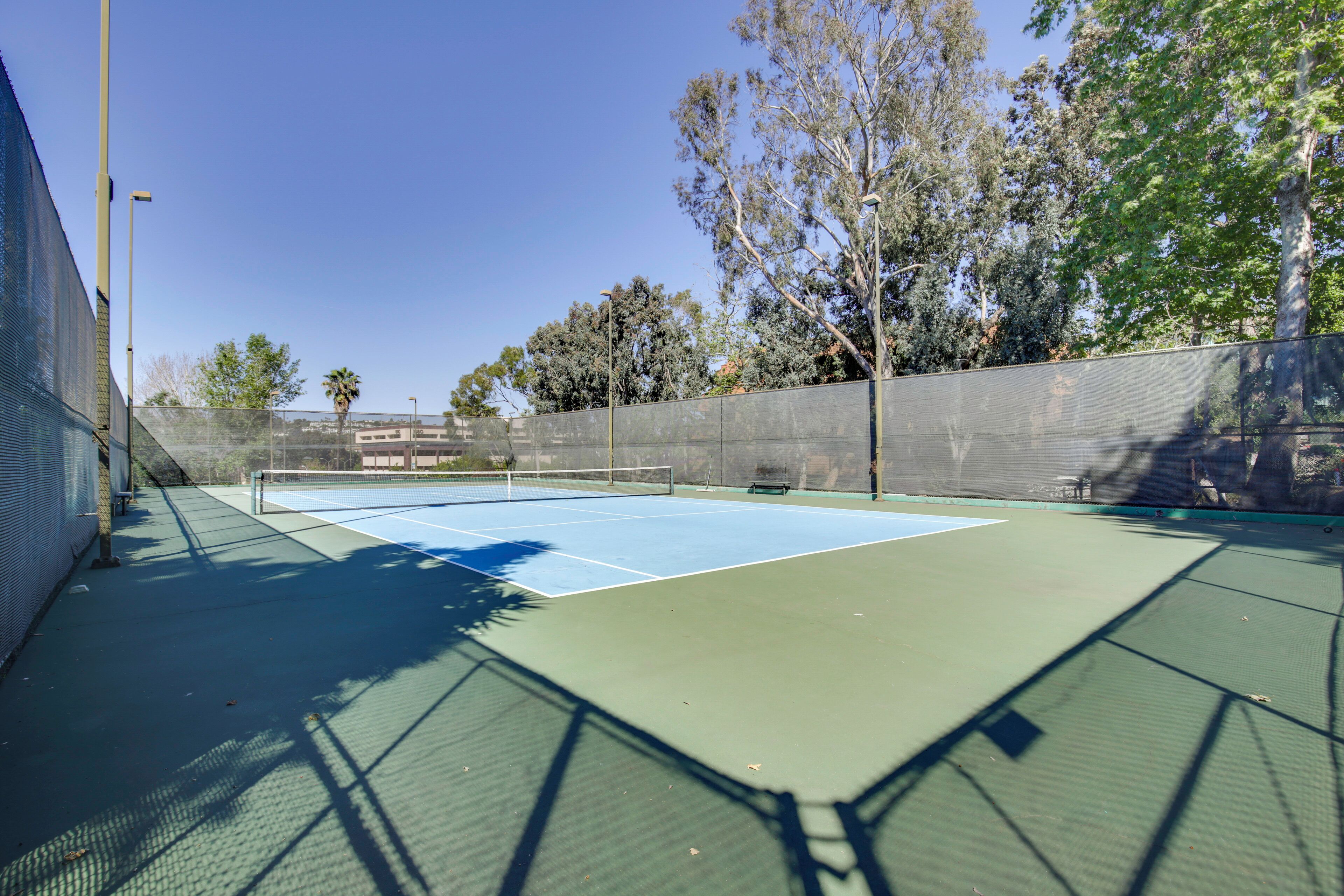 Una cancha de tenis al aire libre con una red, rodeada de árboles y una valla.