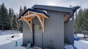 En liten, mörk trästuga med en veranda, en dörr och ett fönster.