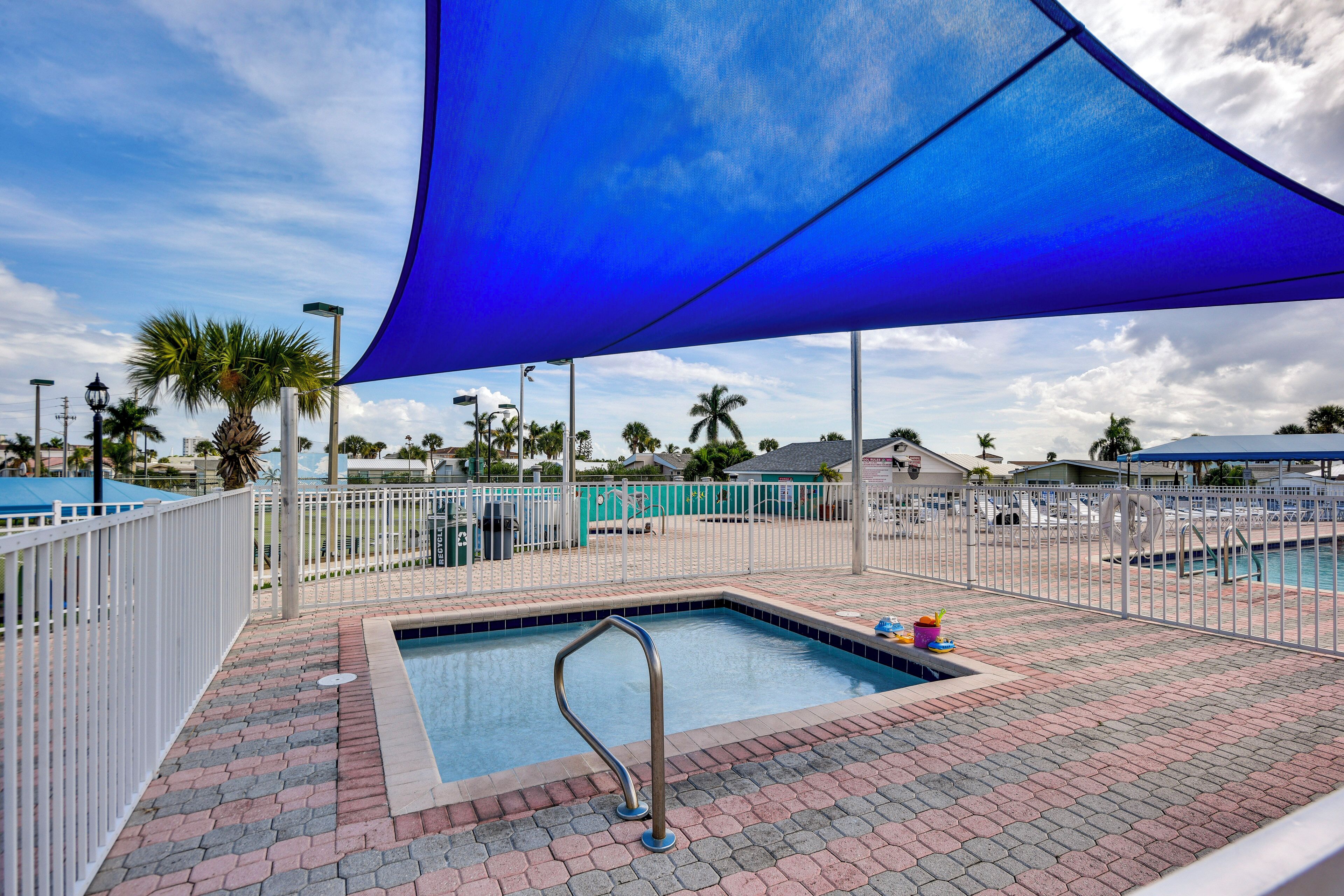 A swimming pool area with a blue shade sail, a pool ladder, and a brick pathway.