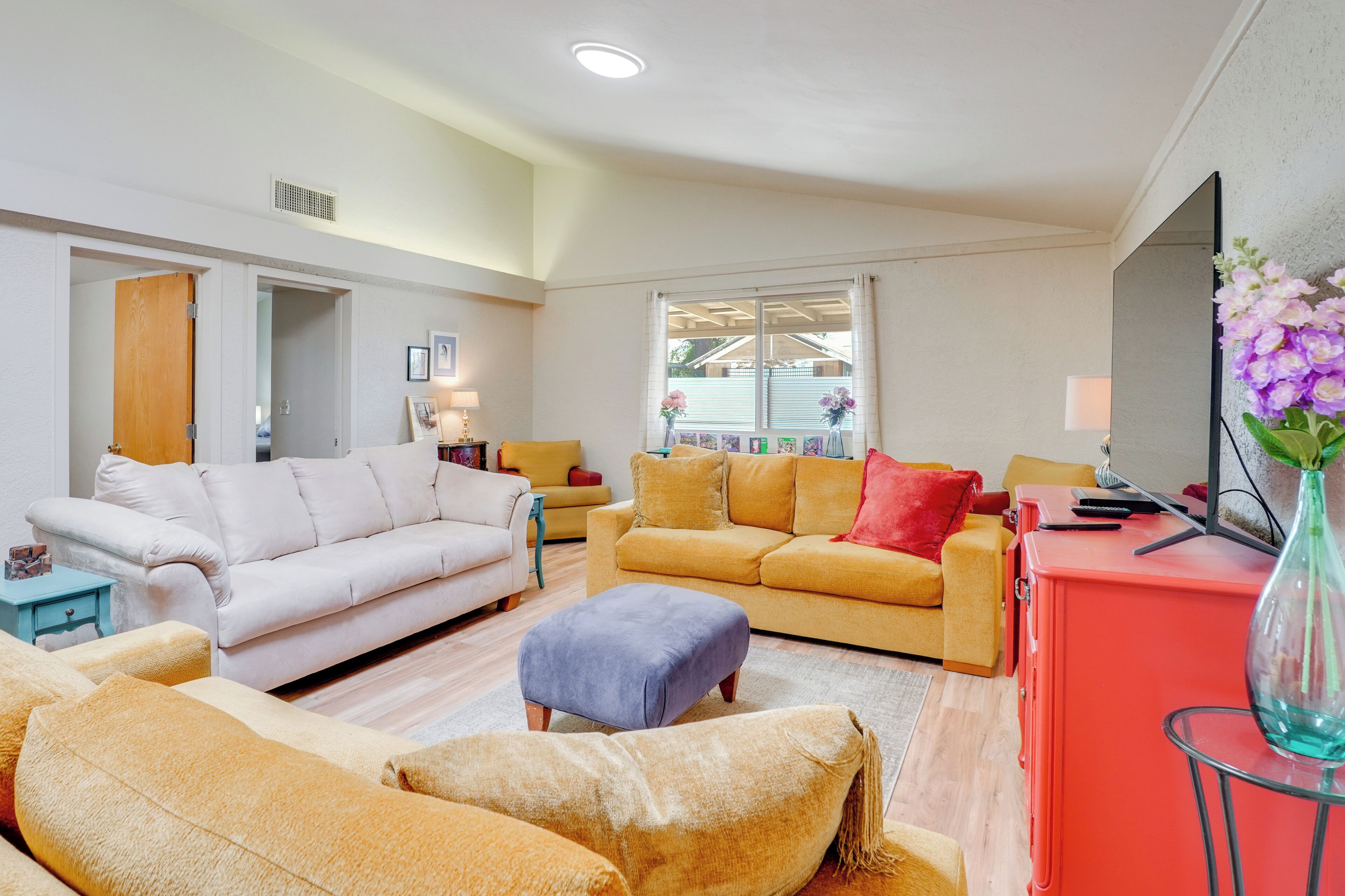 A living room with a white sofa, a yellow sofa, a red cabinet, and a glass table with a vase.