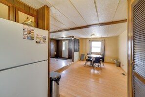 A room with a wooden floor, a dining table with chairs, a refrigerator, and a trash can. - Outdoor Adventure Base in the Heart of Miller (Miller)