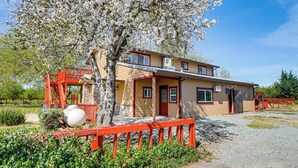 A two-story building with a red exterior, a covered porch, and a tree with white blossoms in front.