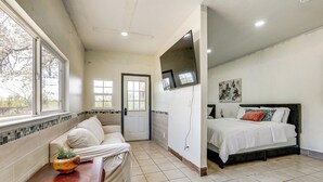 A bedroom with a bed, a TV mounted on the wall, a window, and a door.