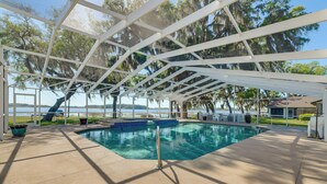 A covered swimming pool with a view of the water and trees. - Lake Days + Pool Fun! Nature Coast Retreat (Hernando)