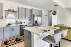 A modern kitchen with grey cabinets, a stainless steel refrigerator, a dining area with a white table, and a green sofa. - Unwind in Kissimmee! Rural Retreat for Families (Kissimmee)