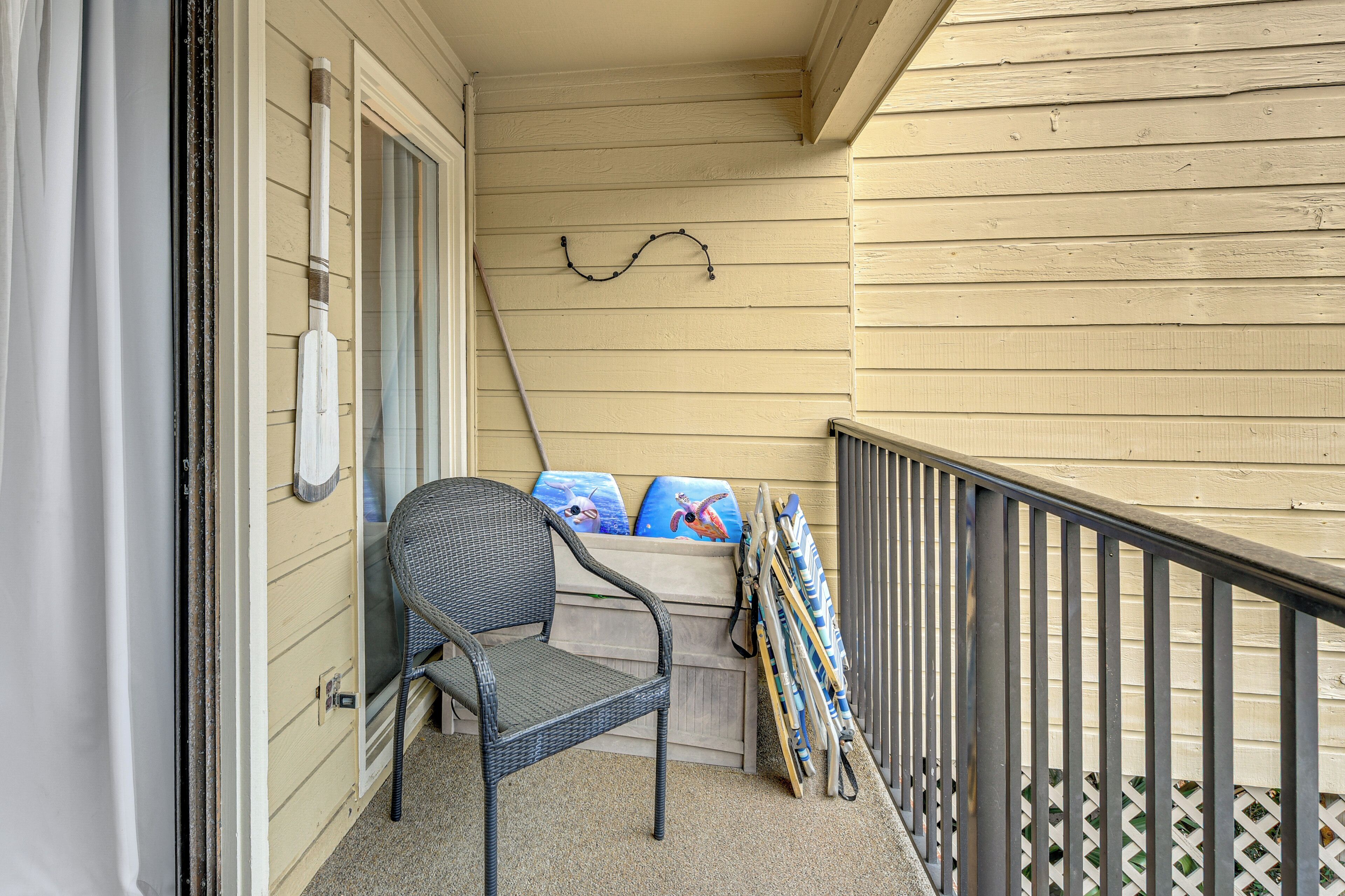 Un balcon avec une chaise, des planches de surf et un porte-planches fixé au mur.