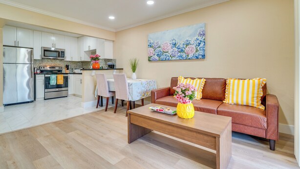 A modern kitchen with stainless steel appliances, a dining area with a table and chairs, a living room with a sofa and coffee table, and a floral painting on the wall. - Walkable Pleasanton Condo Near Downtown w/ Balcony (Pleasanton)
