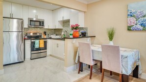 A kitchen with white cabinets, stainless steel appliances, a dining area with a table and chairs, and a painting on the wall. - Walkable Pleasanton Condo Near Downtown w/ Balcony (Pleasanton)