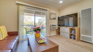 A living room with a sofa, a coffee table with a tray, a TV, a large window with curtains, and a balcony. - Walkable Pleasanton Condo Near Downtown w/ Balcony (Pleasanton)