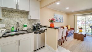 A modern kitchen with white cabinets, a dishwasher, and a coffee maker. There is a dining area with a sofa and a coffee table. - Walkable Pleasanton Condo Near Downtown w/ Balcony (Pleasanton)