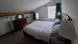 Ein Schlafzimmer mit Bett, Kommode, Lampe, Fenster und Heizkörper.