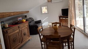 Ein gemütlicher Wohnbereich mit einem Holzkasten, einer Couch, einem Esstisch mit Stühlen, einem Fernseher und einem Fenster mit Blick.