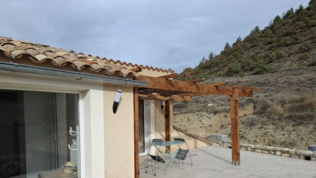 Ein Haus mit Ziegeldach, einer Pergola und einer Terrasse mit Sitzgelegenheiten.