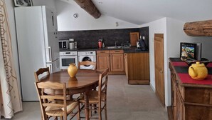 Eine Küche mit Holzausstattung, einem Esstisch mit Stühlen, einem Kühlschrank, einer Mikrowelle, einer Waschmaschine und einer Kaffeemaschine.