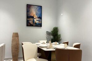 Un comedor con una mesa dispuesta para cuatro, un alto jarrón tejido y un cuadro en la pared.