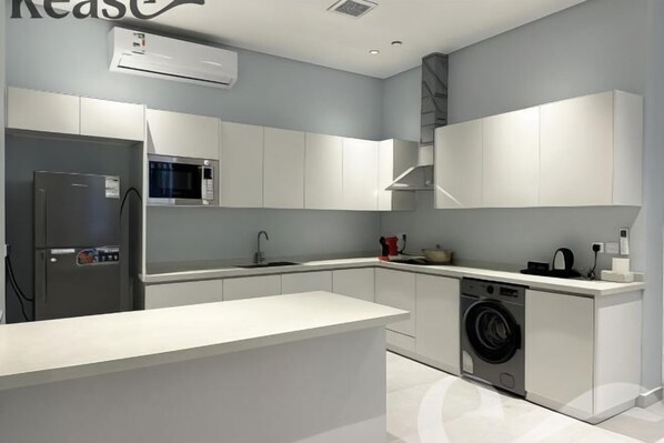 A modern kitchen with white cabinetry, a built-in microwave, a stainless steel refrigerator, and a washing machine. - Kease Ar Rabi J-1 Royal Touch GX69 (Riyadh)