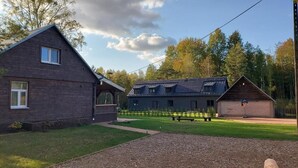 A two-story building with a sloped roof, a small attached structure, and a paved area with a bench. - Olszówka (Goniądz)