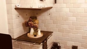 A corner kitchen with white brick walls, a built-in stove, and a wooden shelf above. - Olszówka (Goniądz)