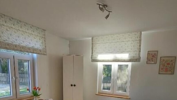 A bedroom with a bed, a wardrobe, a window with a view, and a small table with a vase. - Olszówka (Goniądz)