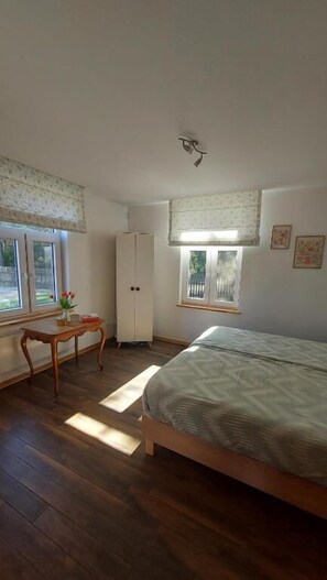 A bedroom with a bed, a wardrobe, a window with a view, and a small table with a vase. - Olszówka (Goniądz)