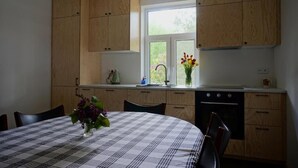A kitchen with wooden cabinets, a window, a dining table with a checkered tablecloth, and a vase with flowers. - Olszówka (Goniądz)
