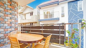 A balcony with a wooden table and chairs, a stone wall, and a building with a blue and white facade.