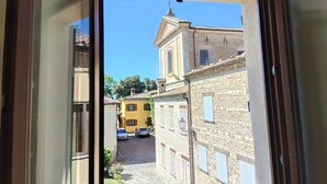Blick durch ein Fenster auf eine enge Straße mit Gebäuden, einer Kirche und parkenden Autos.