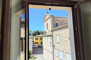 Vista a través de una ventana de una calle estrecha con edificios, una iglesia y coches estacionados.