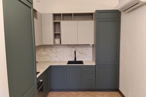 A compact kitchen with a marble countertop, a black faucet, and light-colored cabinets. - Apartment in a village with swimming pool (Pesaro)