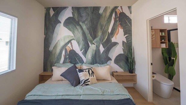A bedroom with a large bed, a nightstand, a wall-mounted shelf, and a view of a bathroom.