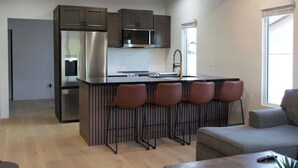 A modern kitchen with a central island, bar stools, and a dining area with a sofa.