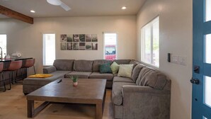 A living room with a sectional sofa, a coffee table, a ceiling fan, and a blue door.
