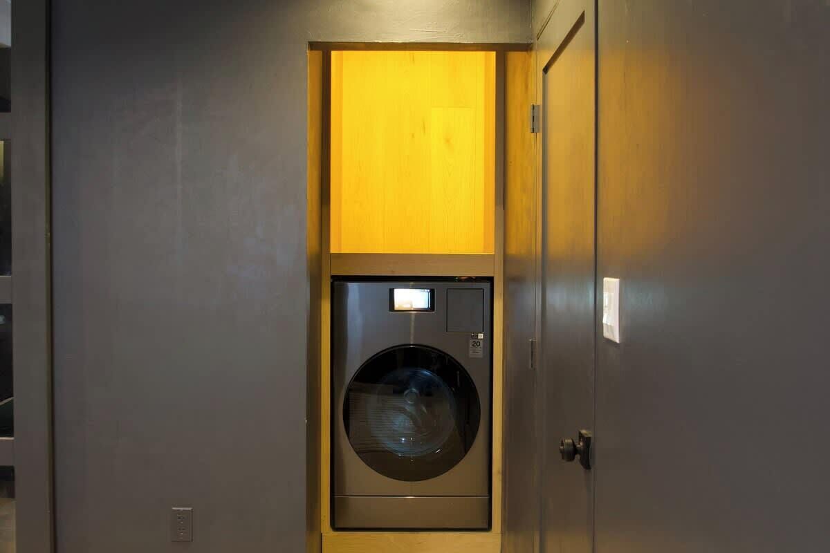 A compact, modern laundry room with a built-in washing machine, a control panel, and a door with a wooden panel.