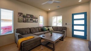 A living room with a sectional sofa, a coffee table, a ceiling fan, and a blue door.