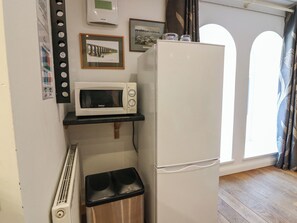 Eine kleine Küche mit einer weißen Mikrowelle, einem kleinen Mülleimer und einem Kühlschrank.