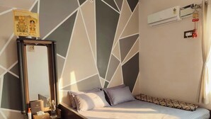 Ein Schlafzimmer mit einem Bett, einem Nachttisch mit Lampe, einem Spiegel und einem geometrischen Wandmuster.