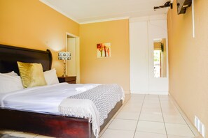 Een slaapkamer met een bed, nachtkastje, lamp en een schilderij aan de muur.
