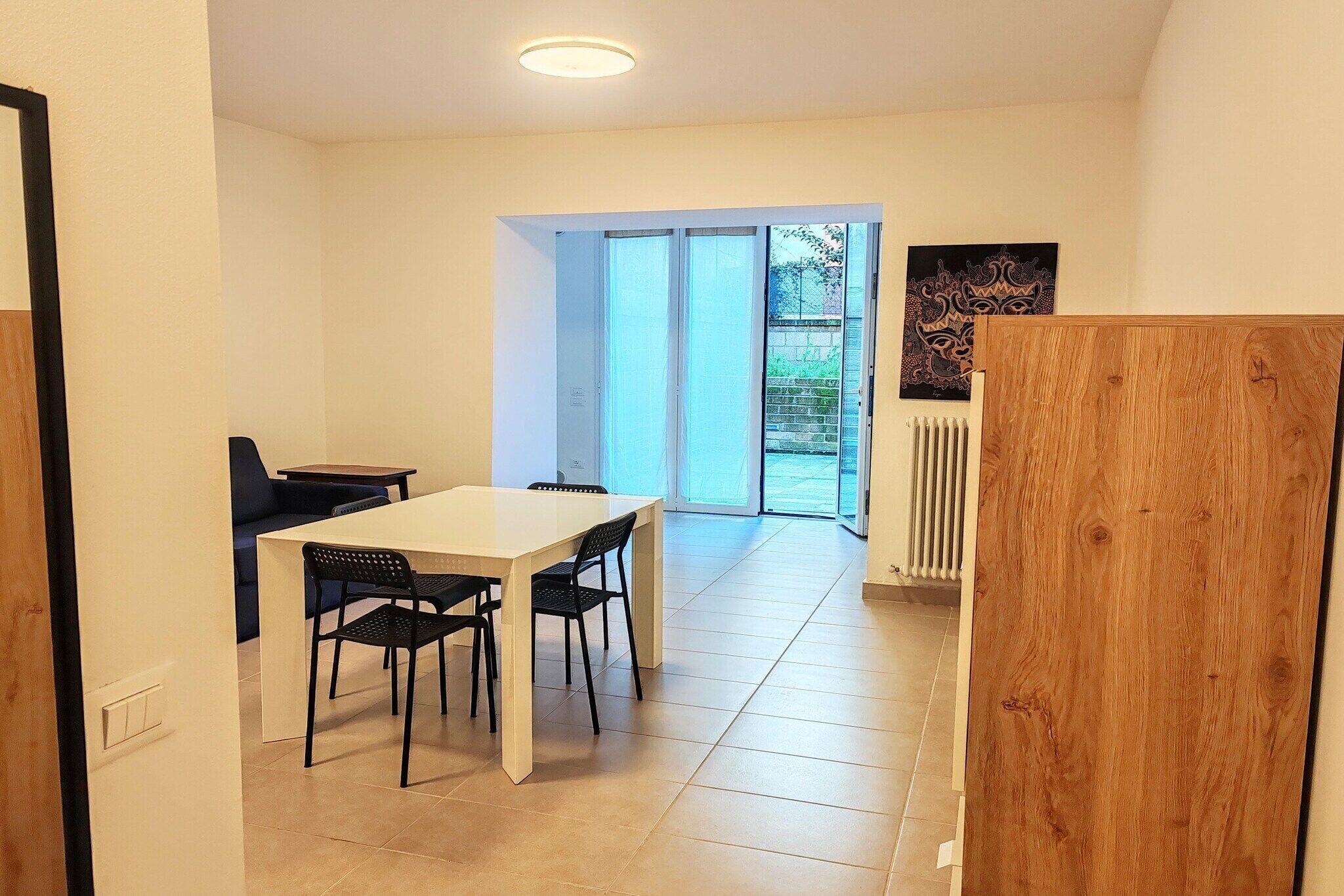 A dining area with a white table and black chairs, a wooden partition, and a view through a glass door to an outdoor space.