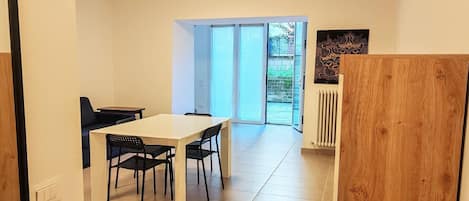 A dining area with a white table and black chairs, a wooden partition, and a view through a glass door to an outdoor space.