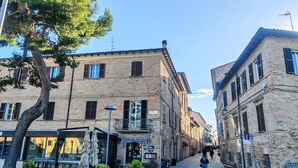 A cobblestone street with buildings, a tree, and a person walking. - Apartment a few minutes from the sea (Fano)