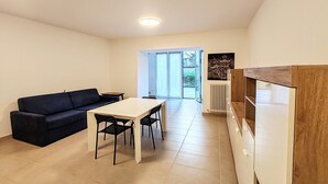 A modern living room with a sofa, dining table, chairs, and a large window. - Apartment a few minutes from the sea (Fano)