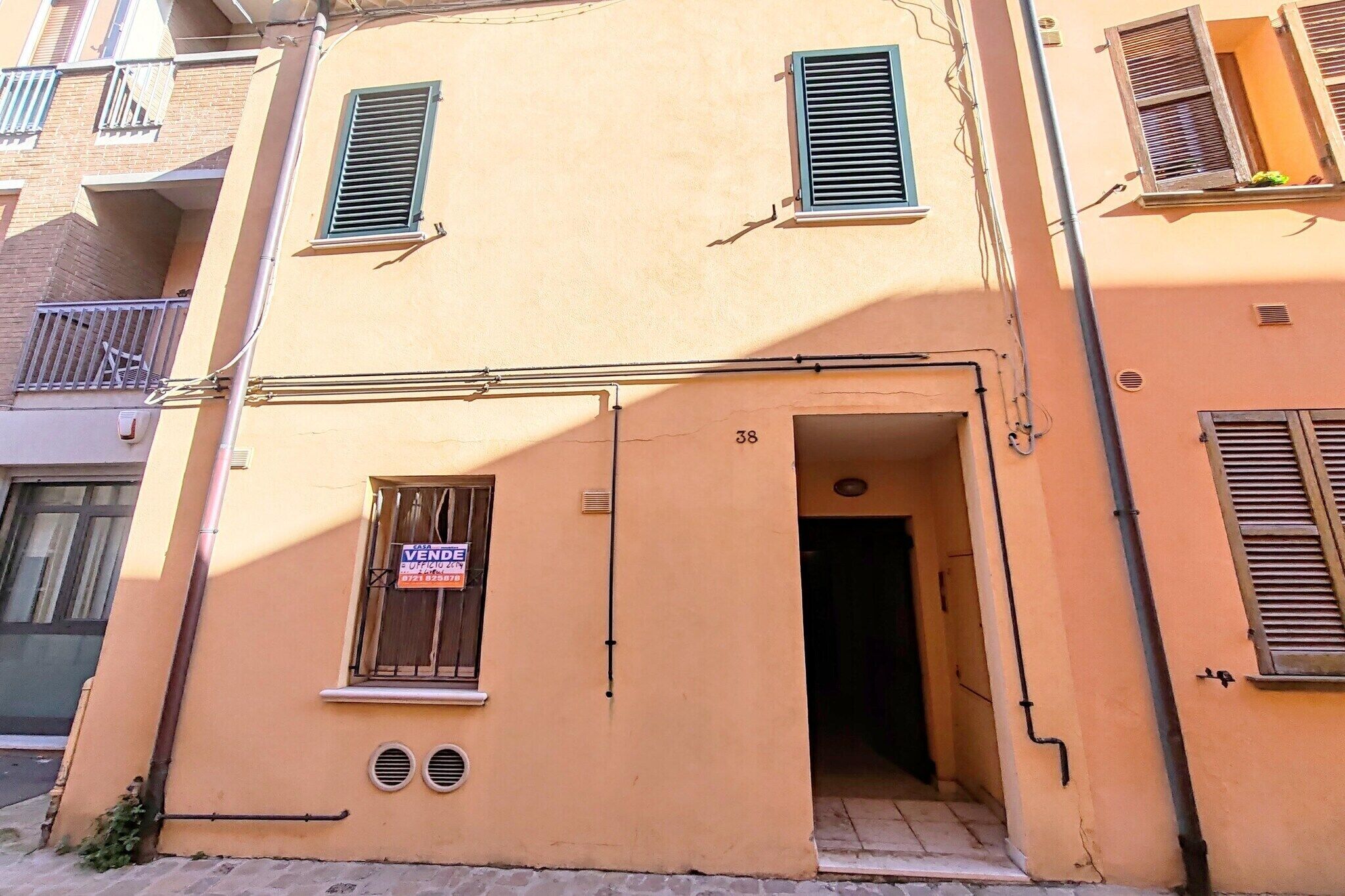 A building with a door marked 'VENDESI,' a window with shutters, and a small vent.