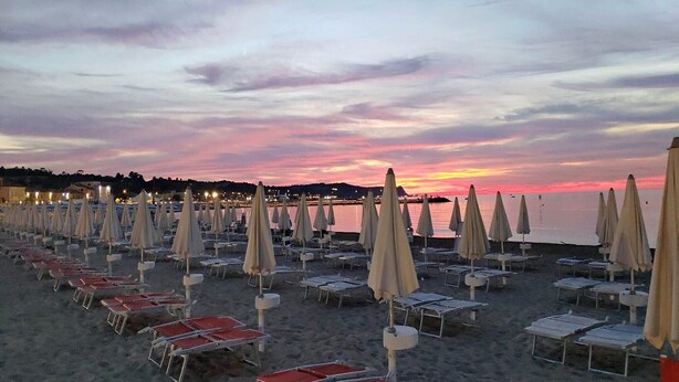 A beach with rows of sun loungers and umbrellas, a sunset in the background, and a calm sea. - Apartment a few minutes from the sea (Fano)