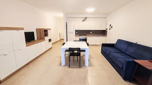 A modern kitchen with white cabinets, a dining table with chairs, and a blue sofa. - Apartment a few minutes from the sea (Fano)