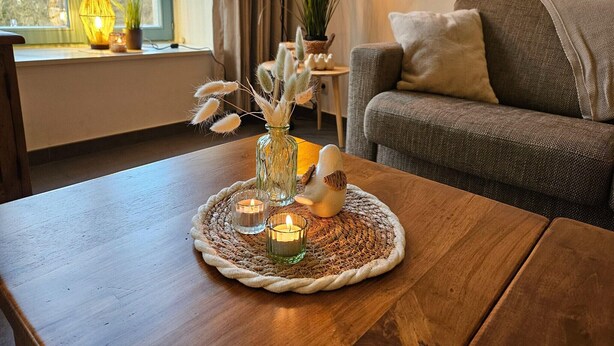 A wooden table with a woven placemat, a glass vase with dried plants, and candles.