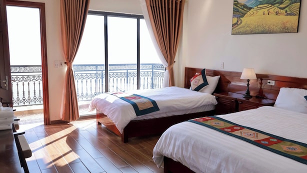 A hotel room with two beds, a balcony with a view, and a painting on the wall. - An Hotel (Sa Pa)