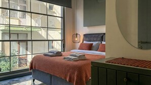 Ein Schlafzimmer mit großem Fenster, einem Bett mit roter Decke, einem Nachttisch und einem Kleiderschrank.