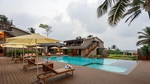A poolside area with lounge chairs, umbrellas, and a building with a staircase. - Sstella Empire Beach Resort, a member of Radisson Individuals (Calangute)